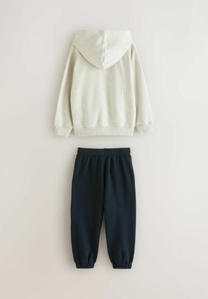 Lysbeige hættepullover og sorte joggerbukser med elastiske manchetter, lagt fladt på en lys baggrund, der viser bagsiden.