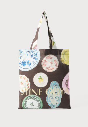 Καφέ τσάντα ώμου με πολύχρωμα σχέδια από vintage πιάτα και μερικό έντονο κίτρινο κείμενο, με διπλές υφασμάτινες λαβές.