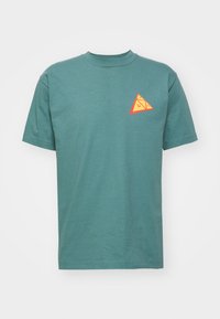 Camiseta de algodón en color teal con mangas cortas, que presenta un pequeño gráfico en forma de triángulo naranja en el lado izquierdo del pecho y un diseño clásico de cuello redondo.