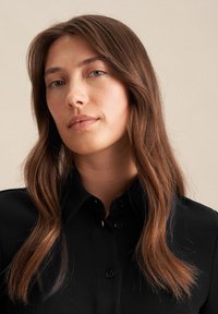 Zwarte button-up overhemd met een spitse kraag en lange mouwen. Gladde textuur, met donkere knopen en minimale ontwerpelementen.