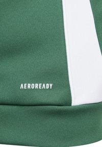 Grüner strukturierter Stoff mit weißem Seitenpaneel, das im unteren Bereich das "AEROREADY"-Logo in Weiß aufweist. Rippbund für zusätzliche Details.
