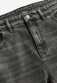 Zwarte denim jeans met een vervaagde textuur, knoopsluiting en zijzakken. Kenmerkt zich door sterke stiksels langs de naden.