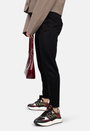 Pantalons noir fuselé, veste cropped marron, sac à main en verni rouge et baskets multicolores avec des textures et motifs variés.