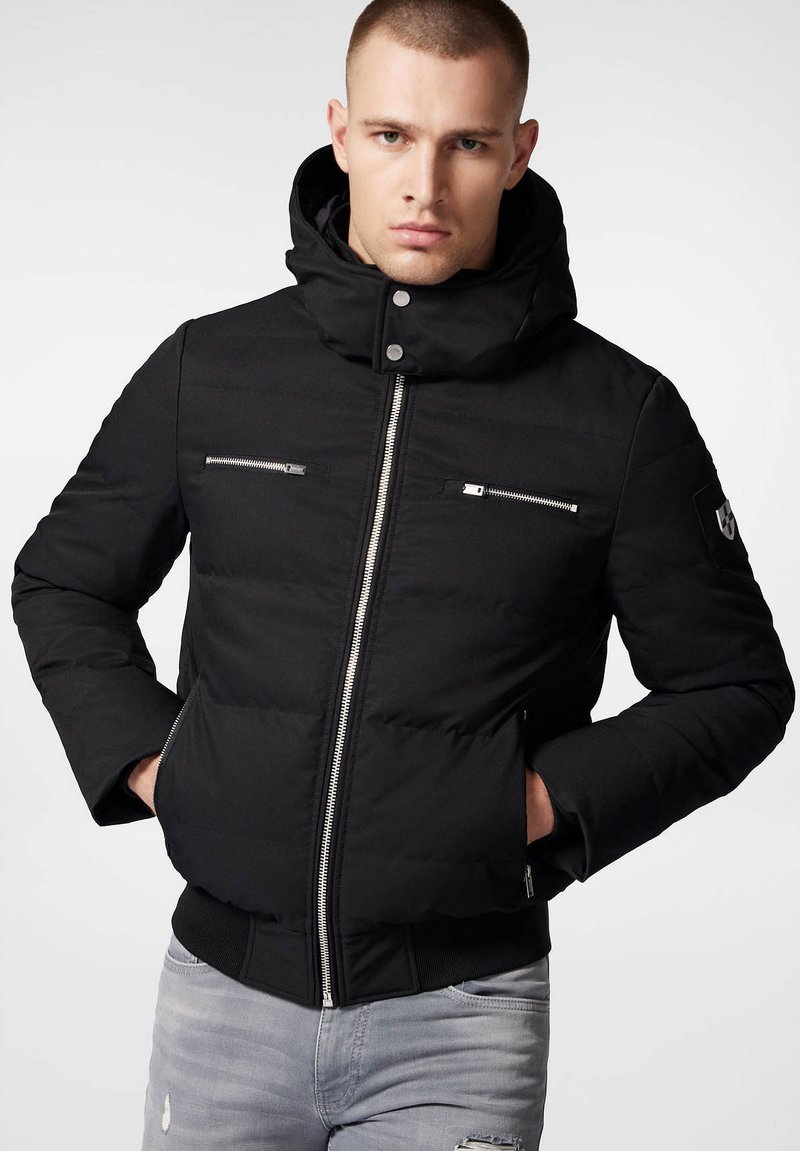 Czarna ocieplana kurtka z wysokim kołnierzem, z przodu na zamek oraz dwoma kieszeniami na piersi z zamkiem błyskawicznym. Posiada ribbowe mankiety i dół.