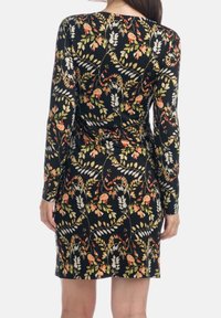 Robe noire à manches longues présentant un motif floral en orange, blanc et vert. Fabriquée en tissu lisse avec une silhouette ajustée et un détail froncé.