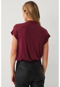 Top corto bordeaux a maniche corte con vestibilità rilassata e scollatura rotonda, abbinato a pantaloni in pelle nera con tasche posteriori e tessuto testurizzato.