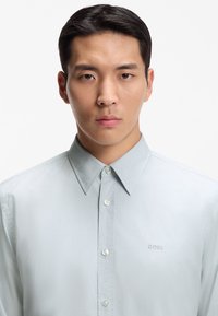 Ανοιχτό γκρι πουκάμισο με κουμπιά, με αιχμηρό γιακά, ομαλή υφή, διακριτική γυαλάδα και κεντημένο λογότυπο "BOSS" στο αριστερό στήθος.