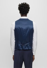 Marineblaues Satin-Weste mit elegantem Rückendesign, verstellbarem Riemen und glatter Textur, kombiniert mit einem weißen Langarmhemd.