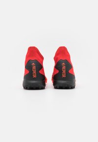 Scarpe da allenamento rosse e nere con una vestibilità aderente, parte superiore testurizzata e suola in gomma modellata con tacchetti per grip. "Predator" arancione sul lato.