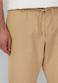 Beige, lichte linnen broeken met een elastische tailleband en koord. Opvallend zachte textuur met zijzakken en een relaxte pasvorm.