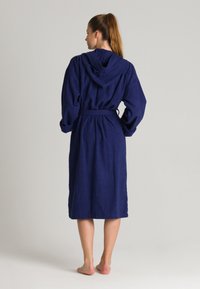 Accappatoio blu navy con cappuccio, cintura e maniche lunghe, realizzato in un morbido tessuto testurizzato, che arriva a metà polpaccio. Senza motivi o accenti visibili.