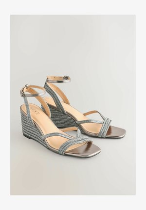 Hõbedased kottjalatsid, mida kaunistavad põimitud rihmad, avatud varvas ja metallilised aktsendid. Omada reguleeritavat pahkluu rihma ja tekstureeritud kottkontsa.