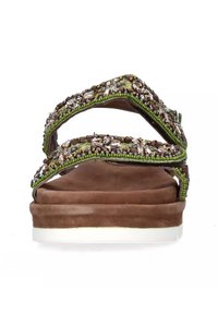 Sandalo marrone con due cinturini incrociati, caratterizzato da perline verdi e cristalli decorativi. Suola piatta con un bordo di colore chiaro.