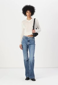 Suéter blanco recortado de punto ligero, combinado con jeans de campana azul claro y zapatos negros, llevando un bolso negro pequeño.
