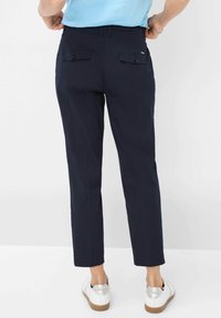 Marineblauwe broek met een rechte pasvorm, voorzien van twee achterzakken en een gladde textuur. Draagt met witte sneakers voor een casual uitstraling.