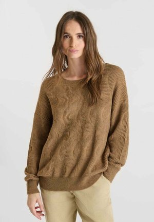 Brown textured sweater with a wavy pattern and a relaxed fit, paired with light-colored corduroy pants. Casual design, long sleeves.