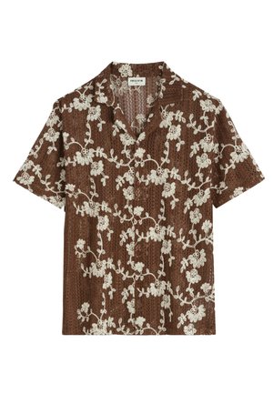 Chemise marron à manches courtes avec superposition de dentelle florale blanche et col pointu, posée à plat sur fond blanc.
