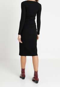 Černé žebrované midi šaty s dlouhými rukávy a přiléhavým střihem, doplněné lesklými vínovými kotníkovými botami s robustním podpatkem.