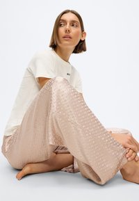 Ροζ σατέν παντελόνι με φαρδιά μπατζάκια, γεωμετρικό υφαντό σχέδιο και λεία επιφάνεια, συνδυασμένο με ένα απλό λευκό μπλουζάκι.