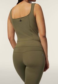 Canotta sportiva verde oliva con scollo a quadrato, design aderente e dettagli di cucitura, abbinata a leggings a vita alta coordinati.