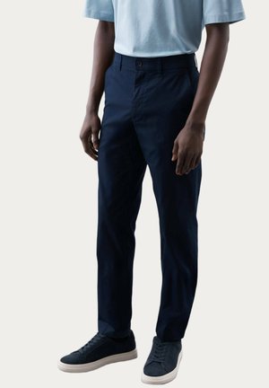 Pantaloni blu navy con una vestibilità dritta, realizzati in tessuto testurizzato, dotati di chiusura frontale con bottone e tasche laterali. Indossati con sneakers grigie.