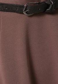 Tela marrón con textura y un cinturón de cuero negro que presenta una hebilla clásica y múltiples orificios para ajuste, acentuando la línea de la cintura.