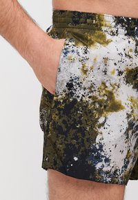 Svømmebukser med et flerfarget søle-mønster i grønt, svart og hvitt, med sidelomme og elastisk midje.