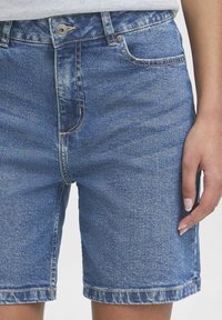 Shorts in denim blu con un lavaggio chiaro, dal taglio dritto, cinque tasche e orli arrotolati, chiusi con un bottone frontale e una cerniera.