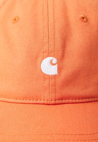 Orange cap made of textured fabric with a curved brim, featuring a white embroidered logo on the side. Structured crown design.