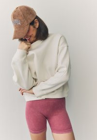 Sudadera color crema de corte holgado, combinada con pantalones cortos de canalé rosa. Gorra de pana marrón con la palabra "AMOUR" bordada en la parte frontal.