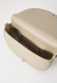 Borsa a spalla in eco pelle beige con patta curva, hardware in argento e un ampio interno dotato di tasca per carte e fodera morbida.