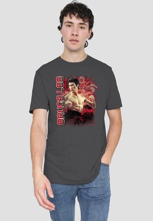 Young man wearing a dark gray t-shirt with a graphic of Bruce Lee in a fighting pose and his name in bold red letters.