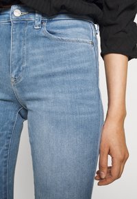 Jeans de denim azul claro con un diseño ajustado, que cuentan con un cierre de botón y cremallera, cinco bolsillos y sutiles detalles de costura.