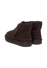 Brązowe zamszowe botki za kostkę o miękkiej fakturze, wyposażone w pasek na rzep i płaską gumową podeszwę, zaprojektowane z myślą o komforcie i łatwości noszenia.