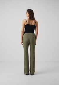Black tank top and olive green, wide-leg pants with textured fabric. The pants feature a high waistband and fall to ankle length.