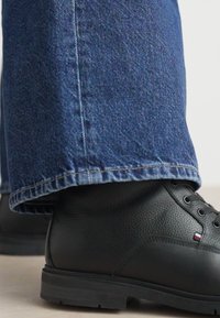 Bottes en cuir noir avec finition texturée, associées à un jean en denim bleu avec une coupe droite et des bords ourlés.