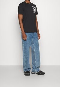 Svart bomullströja med vitt grafiskt tryck, ihopparad med ljusblå vida jeans och svarta sneakers med vita detaljer.