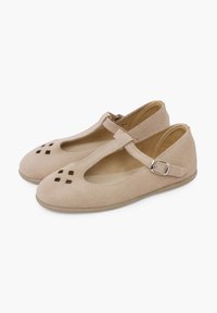 Zapatos de ante beige con correa T y hebilla, que presentan patrones cuadrados recortados en la punta. Diseño de punta redonda y suela plana.