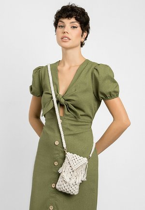 Zielona sukienka z tkaniny z węzłem w talii. Posiada kremową torbę crossbody z makramé, z frędzlami i plecionym wzorem.