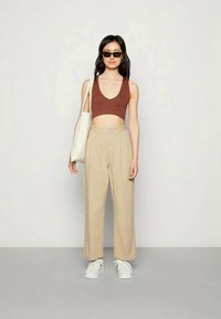 Top crop castanho, calças de perna larga de cintura alta bege, ténis brancos e uma mala tote branca. Acessórios com óculos de sol escuros.