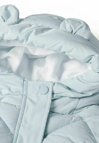 Világoskék steppelt dzseki puha fehér béléssel, lekerekített kapucnival és gombos záródással. Textúrált anyag finom varrási részletekkel.