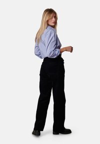 Lichtblauw overhem shirt met opgerolde mouwen, gecombineerd met zwarte corduroy broeken. De outfit heeft een standaard kraag en een relaxte pasvorm.