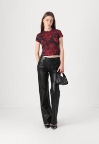 Red graphic short-sleeve top with bold patterns paired with high-waisted black leather pants. Model holds a small black handbag.
