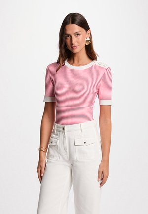 Rood en witte gestreepte top met korte mouwen, ribbelstructuur, ronde halslijn en knopen op de schouders; gecombineerd met witte hoge taille broeken.