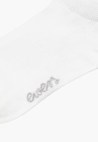Vit bomullssocka med en texturerad toppkant och en liten grå logotyp nära tårna. Materialet är mjukt och lätt.