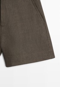 Brune hørshorts med sidelomme og synlige syninger, vist på en hvid baggrund.