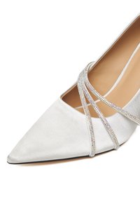 Biały satynowy but z ostrym czubkiem, z trzema cienkimi paskami krzyżującymi się, ozdobionymi małymi błyszczącymi kryształkami.