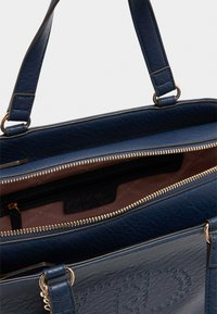 Borsa a mano in pelle blu navy con finitura strutturata, zip dorata e due spallacci. L'interno presenta una fodera beige e una tasca con zip.