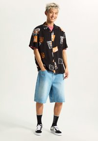 Short-sleeve black shirt with multicolored prints, paired with light blue denim shorts. Worn with black and white checkered sneakers and black socks.