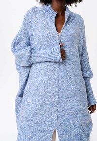 Ljusblå stickad tröja med hög krage, halv dragkedja, ribbade ärmslut och sidorevor för extra rörelsefrihet och komfort.